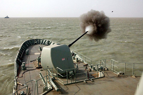 A naval gun firing, white plume of re-condensing propellant gas sticking out from the muzzle