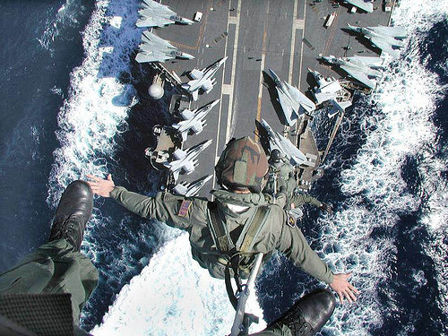 A Navy photographer leaning out over the flight-deck edge above parked F-14 Tomcats