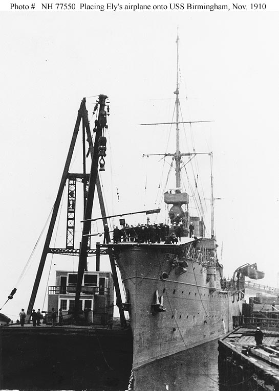 Sailors and civilians crowd around Ely's Curtiss pusher airplane as a floating crane places it on board USS Birmingham at the Norfolk Navy Yard