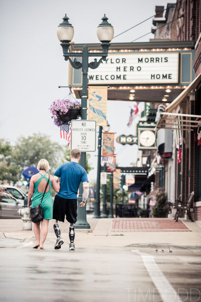 Taylor Morris walking down his hometown street past a theater marquee reading TAYLOR MORRIS HERO WELCOME HOME