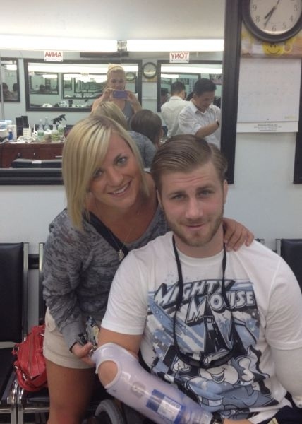 Taylor Morris in a barber chair, his girlfriend leaning over his shoulder, his prosthetic arm across his lap