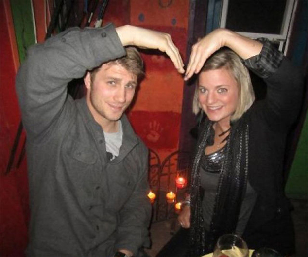 Taylor Morris and his girlfriend at a candlelit table, arms raised together to form a heart above their heads