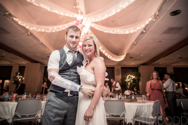Taylor Morris in vest and tie beside his bride at their wedding reception, under strings of lights